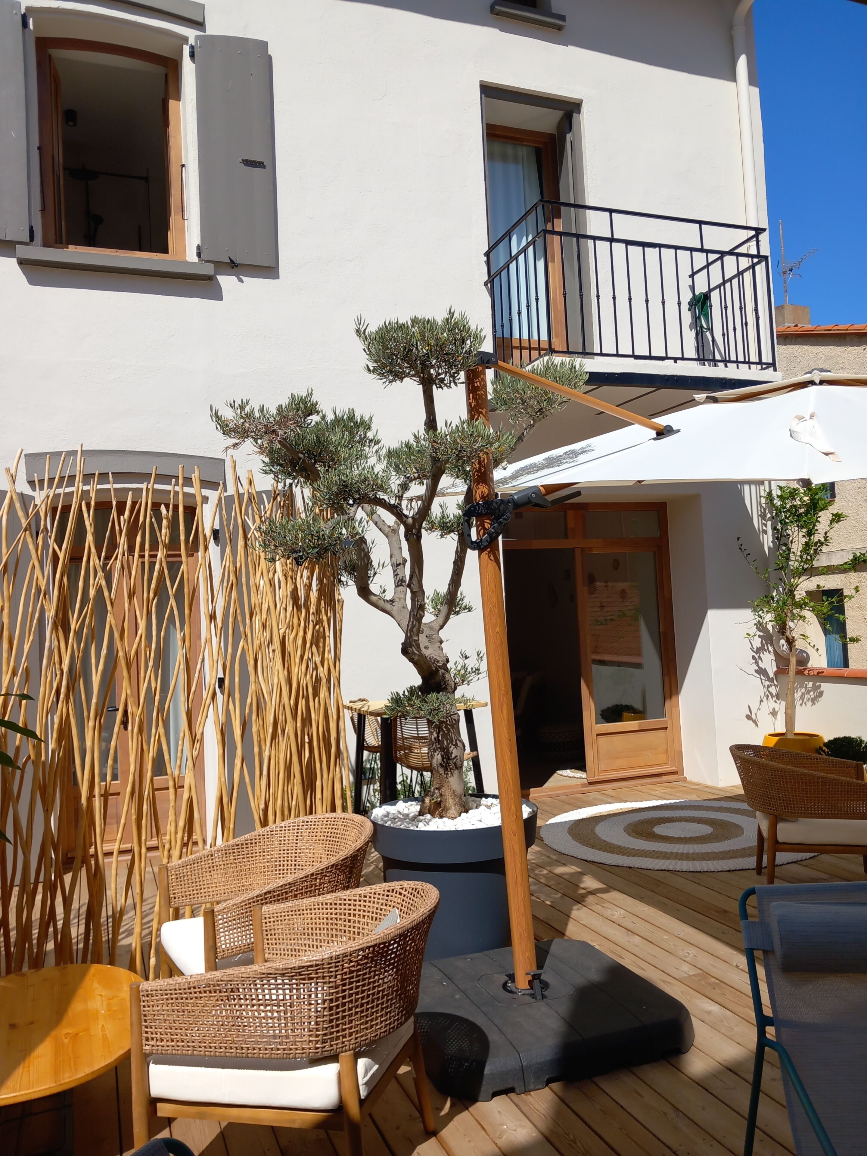 A wooden deck with wicker furniture, a potted tree, and a balcony with a railing.