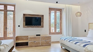 A bedroom with a TV, wooden furniture, a bed with a striped blanket, and large windows. - Intense Boutik Hôtel (Port-Vendres)