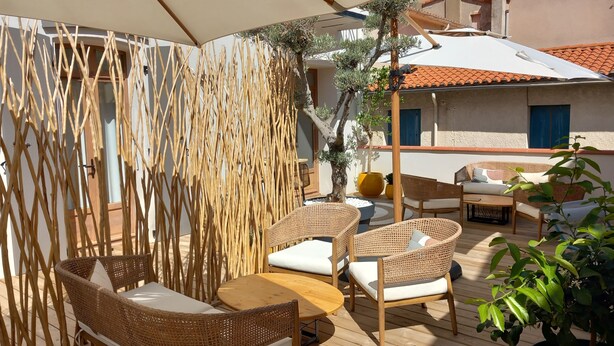 An outdoor seating area with wicker furniture, a wooden table, and a bamboo screen. - Intense Boutik Hôtel (Port-Vendres)