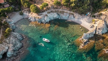An aerial view of a coastal area with a boat on clear turquoise water, rocky terrain, and sparse vegetation.