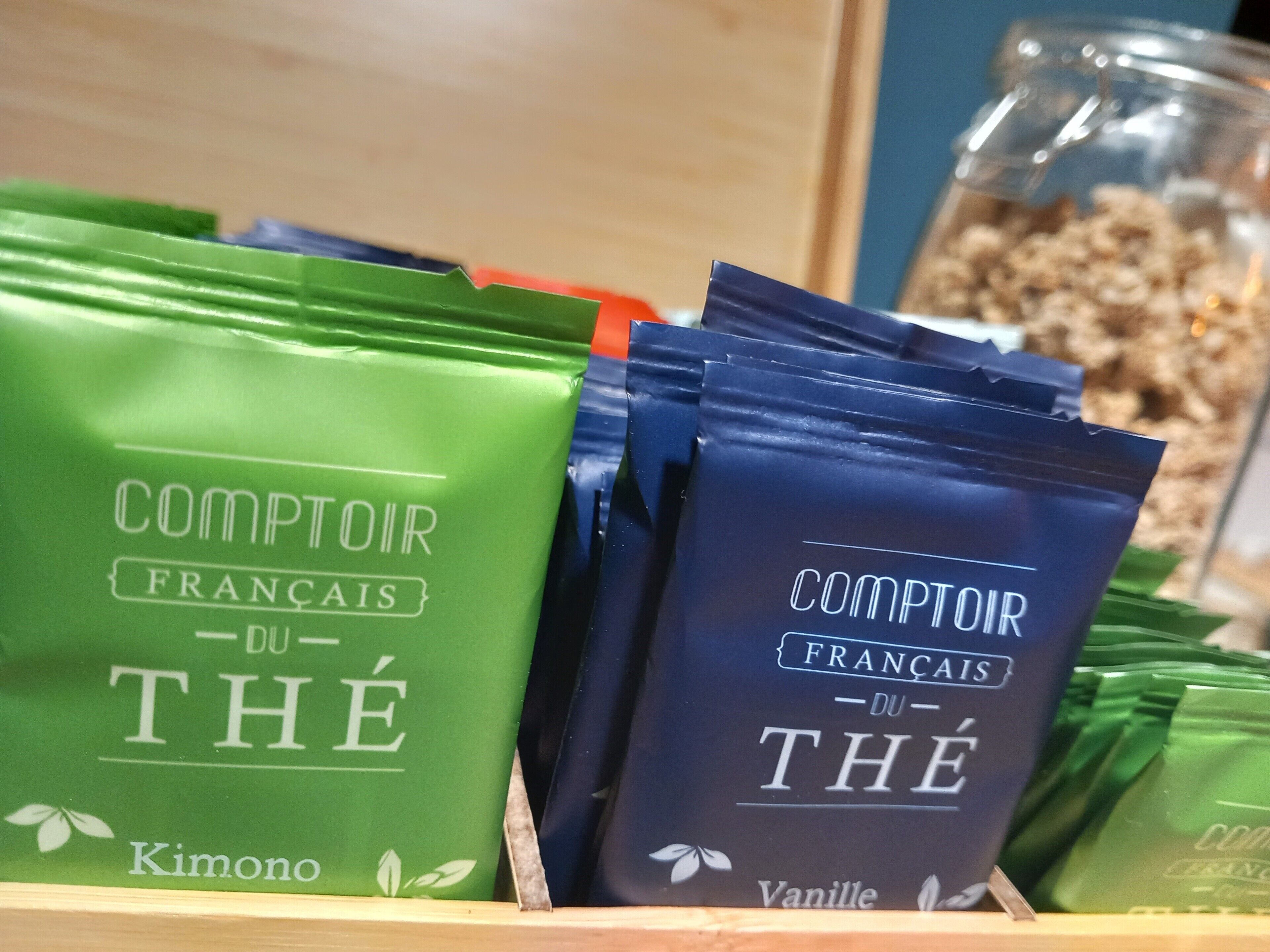 Une exposition de sachets verts et bleus étiquetés « Comptoir Français du Thé », aux saveurs « Kimono » et « Vanille ».