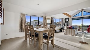 Un amplio espacio de estar con una mesa de comedor, sillas y un sofá. Grandes ventanas ofrecen vistas al exterior.