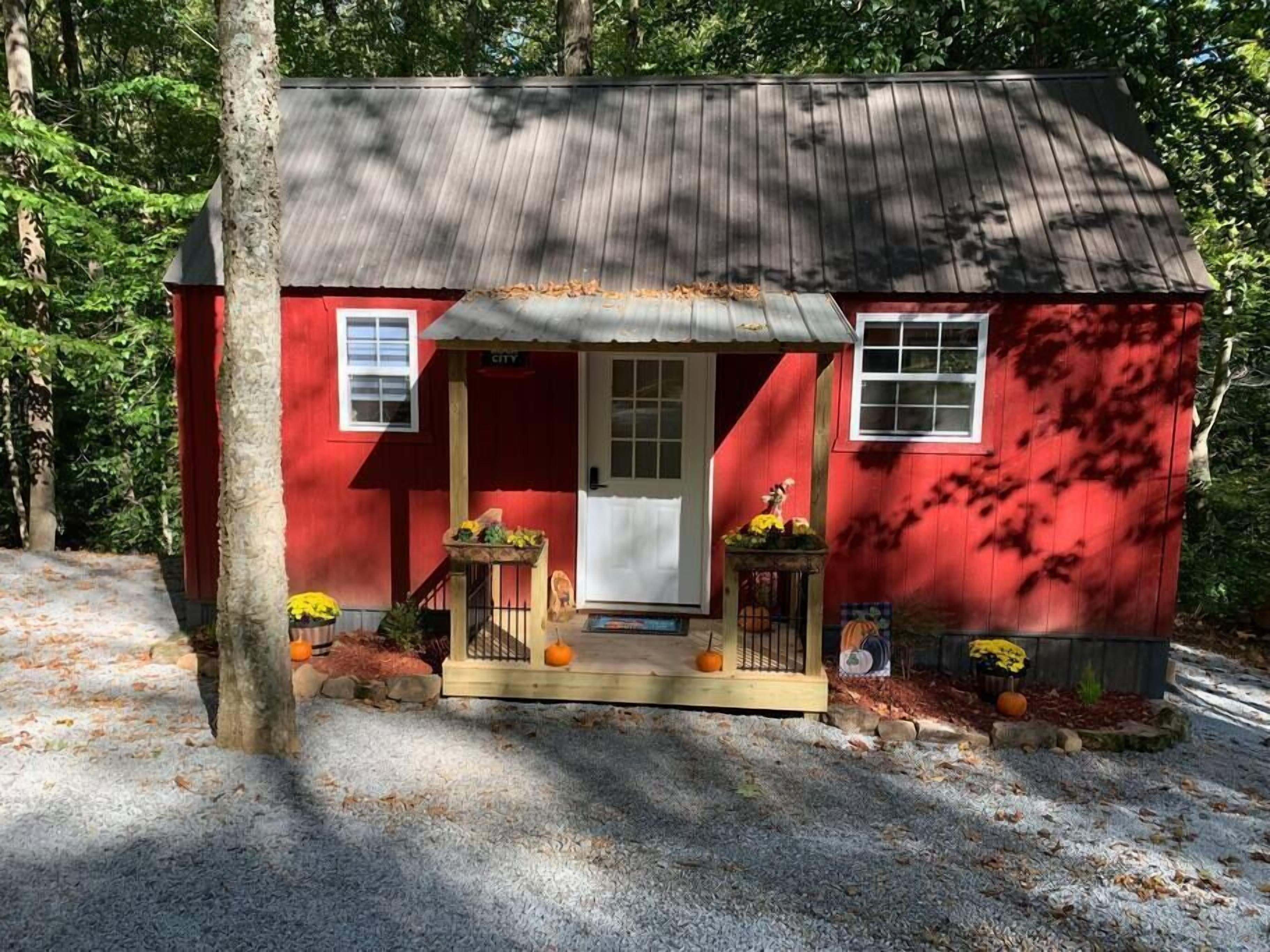 Une petite cabane rouge avec une véranda, une porte et des fenêtres.
