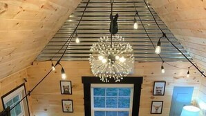 Ein gemütliches Blockhaus-Interieur mit einem Schachbrettmuster-Boden, Holzwänden, einer Kristallleuchtre, gerahmten Bildern und Herbstlaub.