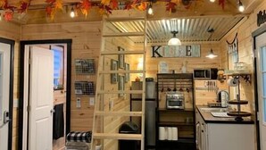 Ein gemütliches, blockhausähnliches Interieur mit Küchenbereich, Holzwänden und einer Leiter, die zu einem Schlafboden führt.