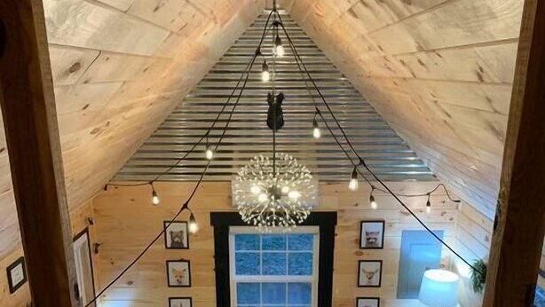 Ein gemütliches Blockhäuschen-Interieur mit kariertem Boden, einer Chandelüster, gerahmten Bildern und Herbstlaub.