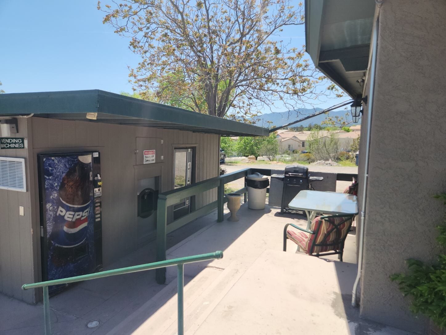 Un petit espace extérieur comprenant un distributeur automatique, une poubelle, un barbecue et une table avec un banc.