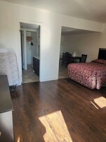Quarto com cama, escrivaninha e cadeira. Há uma porta que dá para um banheiro e um corredor.