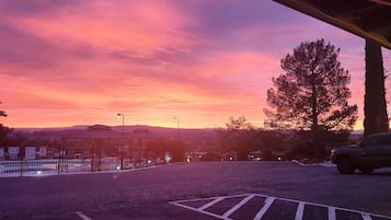 A parking area with a sunset view, a large tree, and a gazebo structure.