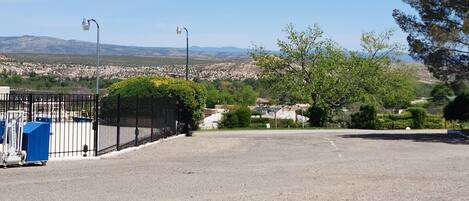 Un parking entouré d’une clôture, avec des lampadaires, et d’où l’on peut apercevoir une ville et des montagnes au loin.