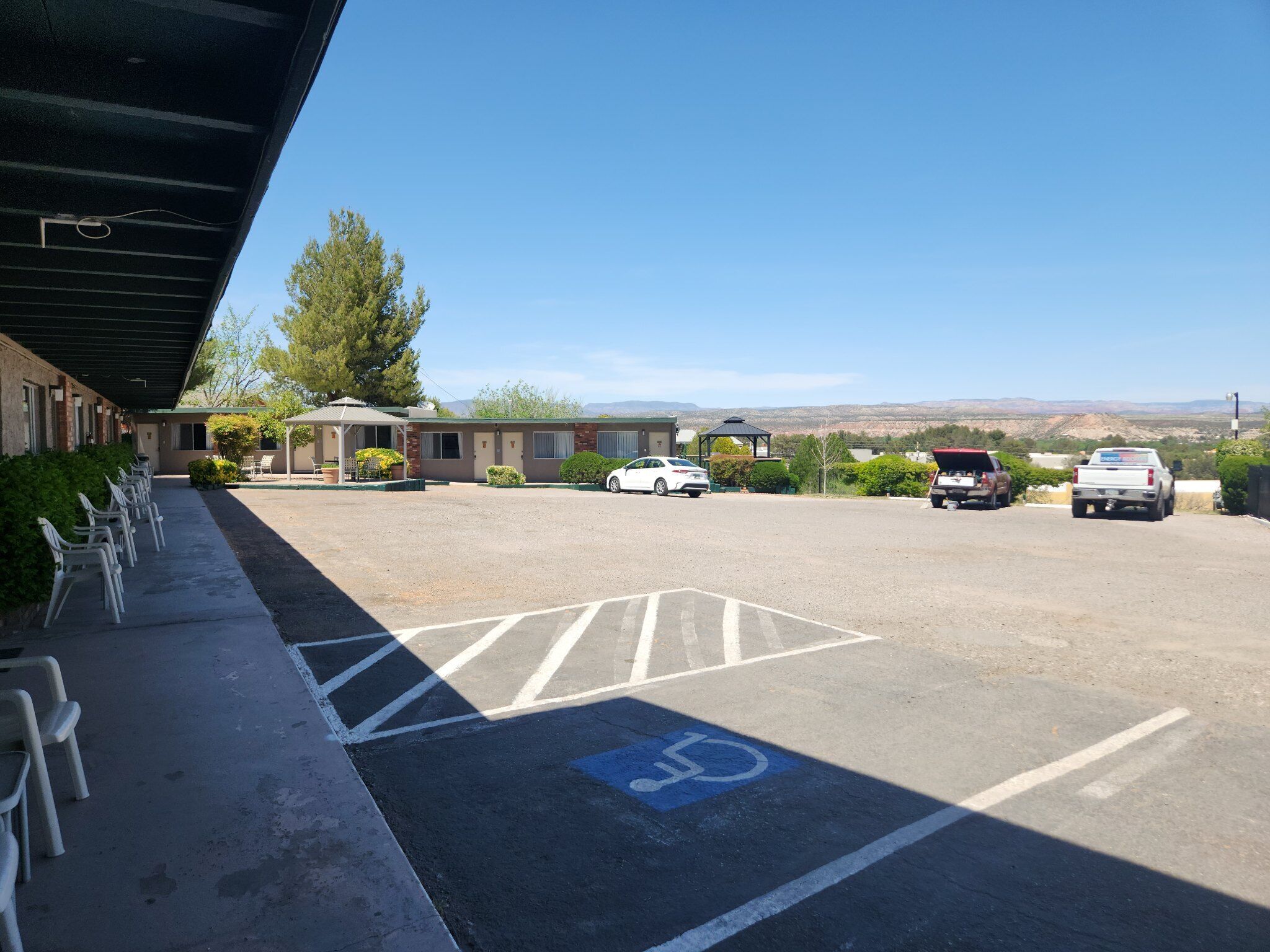 Un parking avec une place réservée aux personnes handicapées, une rangée de chaises en plastique blanches et, au fond, un bâtiment doté d’une zone abritée.