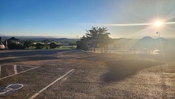 A parking lot with a gazebo and a fence, surrounded by greenery and distant hills.