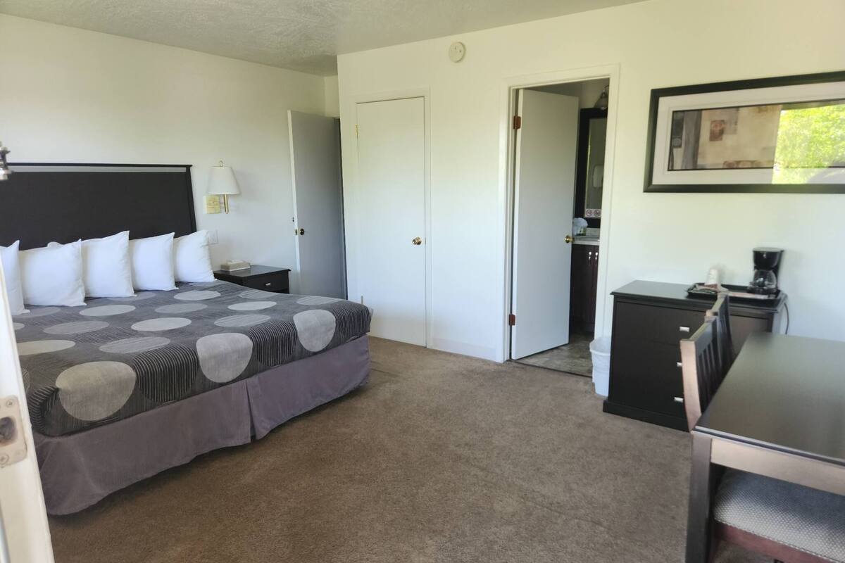 A bedroom with a bed, bedside table, lamp, and a desk with a chair.