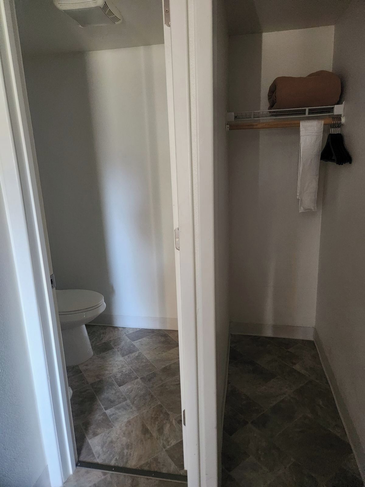 A bathroom with a toilet, a shower area, and a shelf with towels.
