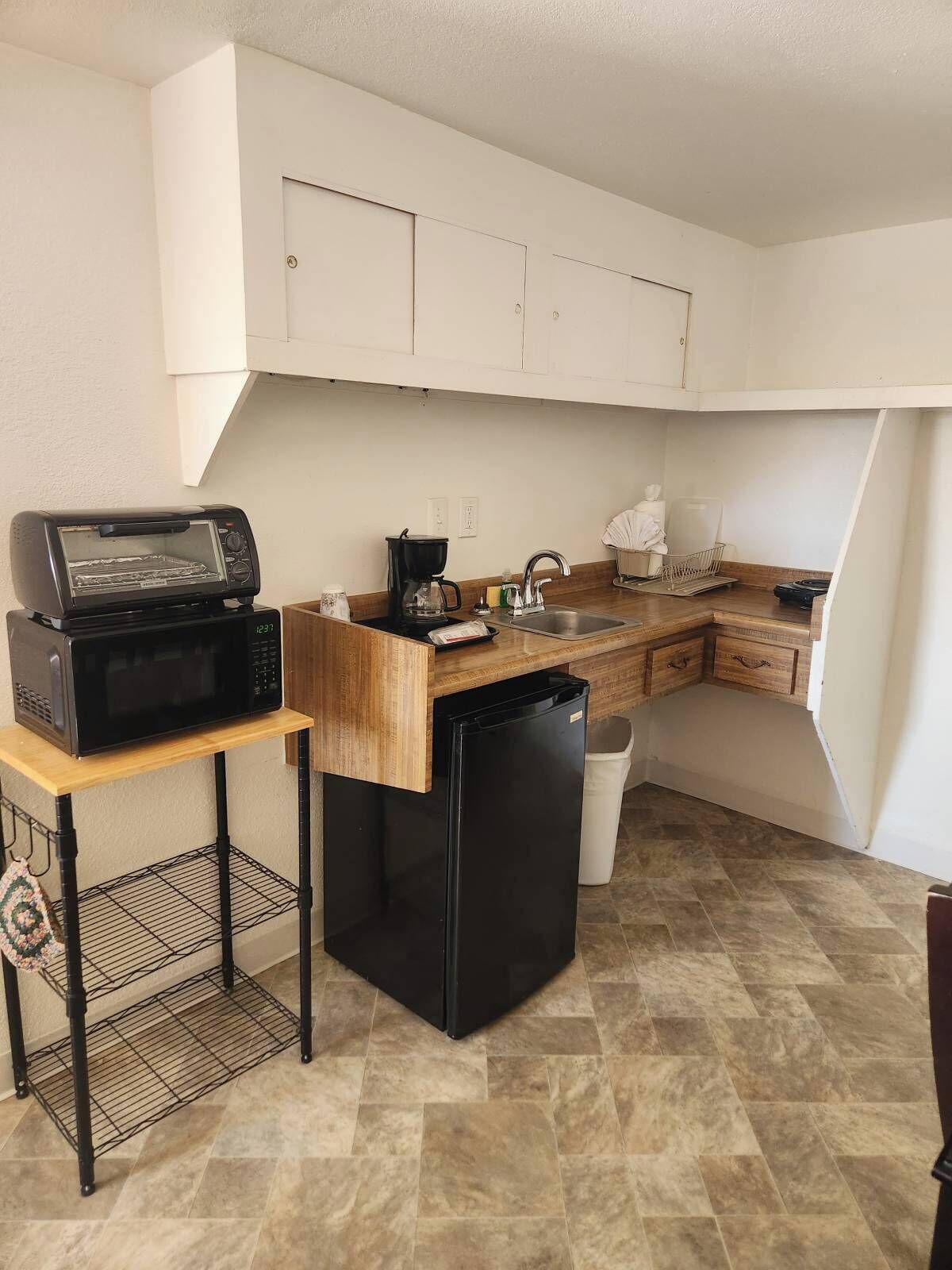 A compact kitchen with a microwave, toaster, coffee maker, and a small refrigerator.