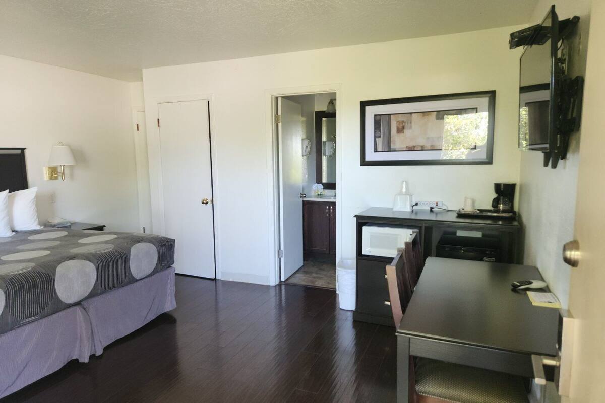 A hotel room with a bed, a desk, a chair, a microwave, a coffee maker, and a framed picture on the wall.