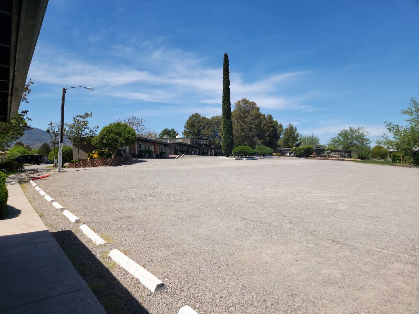 A spacious parking lot with a gravel surface, surrounded by buildings and trees.