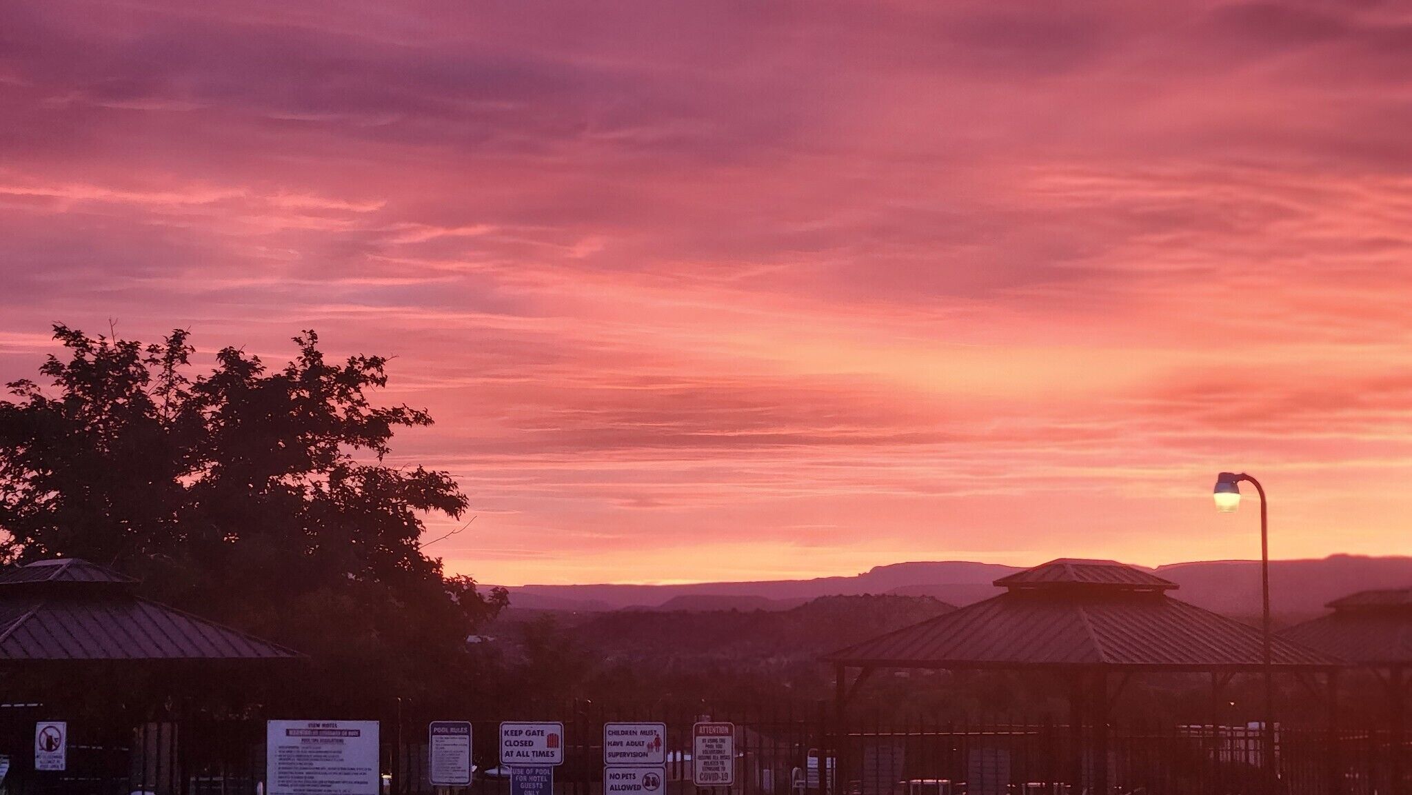 Une vue au coucher du soleil avec un belvédère, un lampadaire et un panneau indiquant que la piscine est fermée.