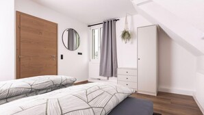 Une chambre avec deux lits, une porte en bois, un miroir, une armoire et une fenêtre avec des rideaux.