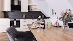 Une cuisine moderne avec des meubles blancs, un plan de travail noir et un coin repas agrémenté d’une table en bois mise pour le repas.