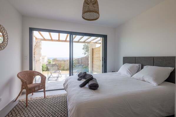 A bedroom with a large bed, a wicker chair, and a view through a sliding glass door to an outdoor area.