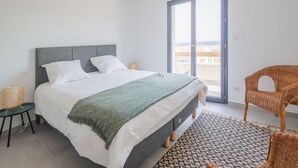 Una camera da letto con un letto, una finestra, una sedia in vimini e un tavolino.