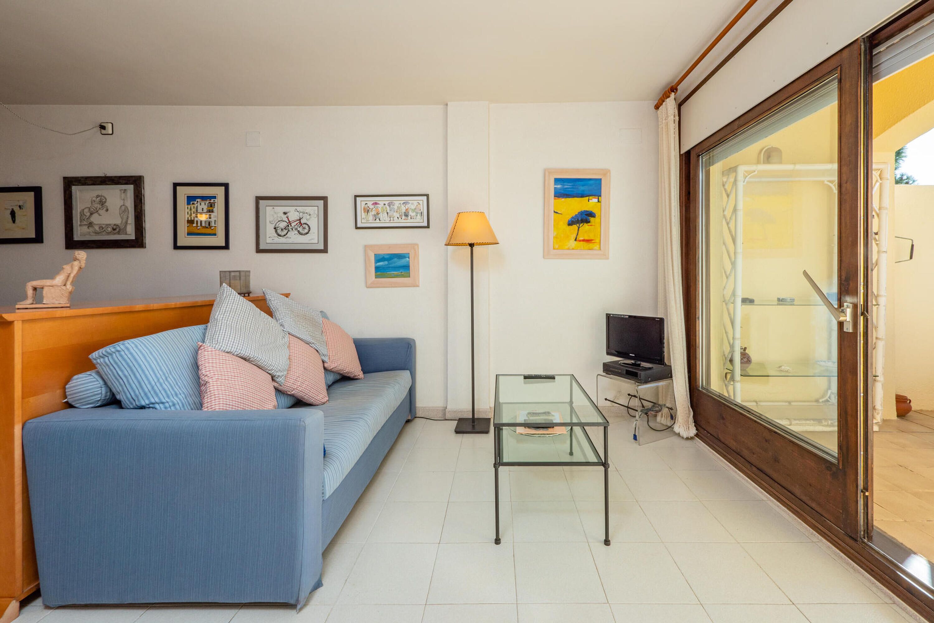 A living room with a blue sofa, a glass coffee table, a TV, and framed artwork on the wall.