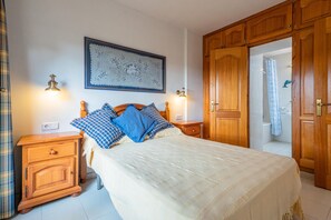 A bedroom with a bed, wooden nightstands, a night lamp, a framed artwork, and a wardrobe.