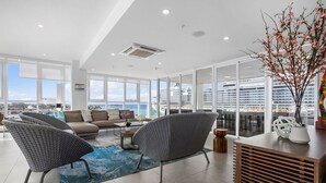 Een moderne woonkamer met uitzicht op een cruiseschip, grote ramen en een blauw tapijt.