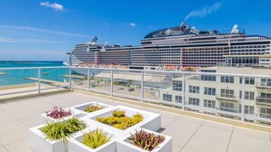 Een cruiseschip ligt aangemeerd in een haven, met een zwembadgedeelte met witte plantenbakken en diverse planten.