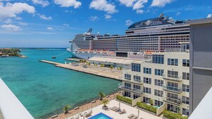 Een groot cruiseschip ligt aangemeerd in een haven, met een modern hotelgebouw ernaast.