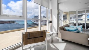 Een moderne woonkamer met grote ramen met uitzicht op een jachthaven en cruiseschepen.
