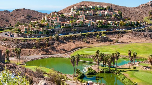 A hillside resort with modern buildings, a golf course, and a body of water.
