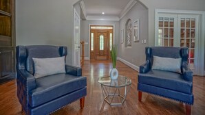 A hallway with two blue leather armchairs, a glass coffee table, and a wooden door at the end. - Hidden Haven on 9 acre, pond, barn and more, sleeps 20 (Stanfield)