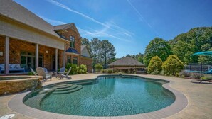 A swimming pool with a curved edge, lounge chairs, and a brick building with a covered patio. - Hidden Haven on 9 acre, pond, barn and more, sleeps 20 (Stanfield)