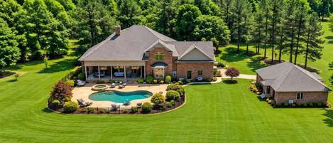 A large house with a swimming pool, surrounded by well-maintained lawns and trees.