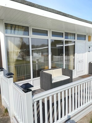 A covered outdoor seating area with a white railing, large windows with blinds, and a door with a mailbox. - Chalet No 30 - Holiday Home From Home! (Skegness)