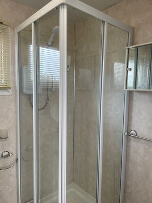 A corner shower with a glass door, a hand dryer, and a towel rack.