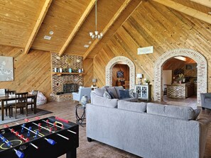 Una sala de estar estilo loft acogedora, con techo alto, vigas de madera a la vista, chimenea, sofá, una mesa de centro y una mesa de futbolín.