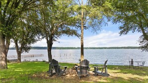 En picknickplats vid sjön med Adirondack-stolar och ett bord, omgiven av träd och med utsikt över sjön.