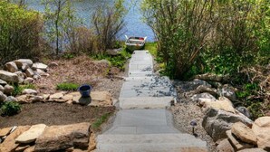 A stone pathway leading to a boat on a lake, surrounded by rocks and greenery. - SO 68 Perch Cove (South Kingstown)