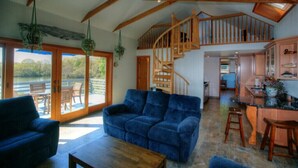 A spacious living area with a blue sofa, wooden coffee table, and a staircase leading to an upper level. - SO 68 Perch Cove (South Kingstown)