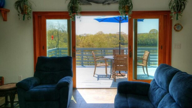 A room with two blue sofas, a small table, and a view of an outdoor deck with a table and chairs. - SO 68 Perch Cove (South Kingstown)
