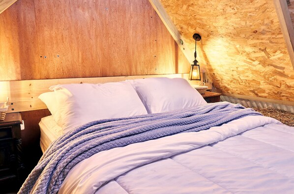 A bed with white linens and a blue knitted blanket, a wooden headboard, and a nightstand with a lamp. - Wabisabi Glamping (Bogotá)