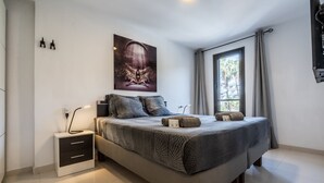 A modern bedroom with a large bed, a bedside table, a wall-mounted artwork, and a window with curtains. - APARTMENT IN VIÑA DEL MAR - PLAYA DE LAS AMERICAS (Costa Adeje)