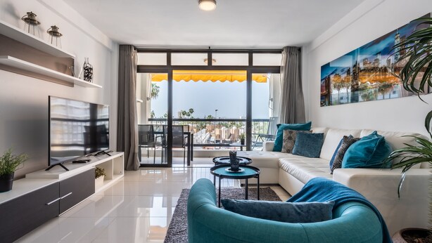 A modern living room with a sofa, TV, and a balcony with a city view. - APARTMENT IN VIÑA DEL MAR - PLAYA DE LAS AMERICAS (Costa Adeje)