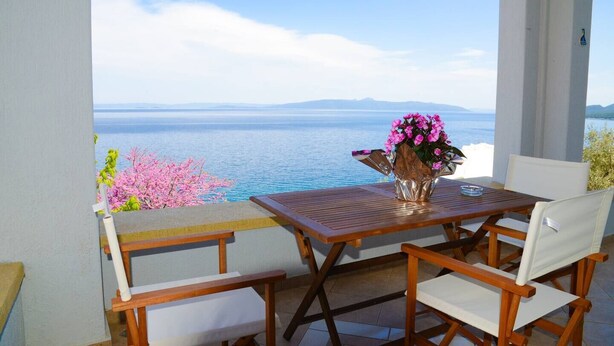 A wooden table and chairs on a balcony with a view of the sea and mountains. - Ira Charming apt with stunning view (Almyros)