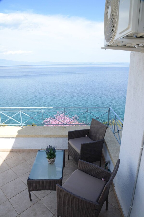 Enjoy the ocean view from this balcony with a glass-top table, two chairs, and a potted plant.