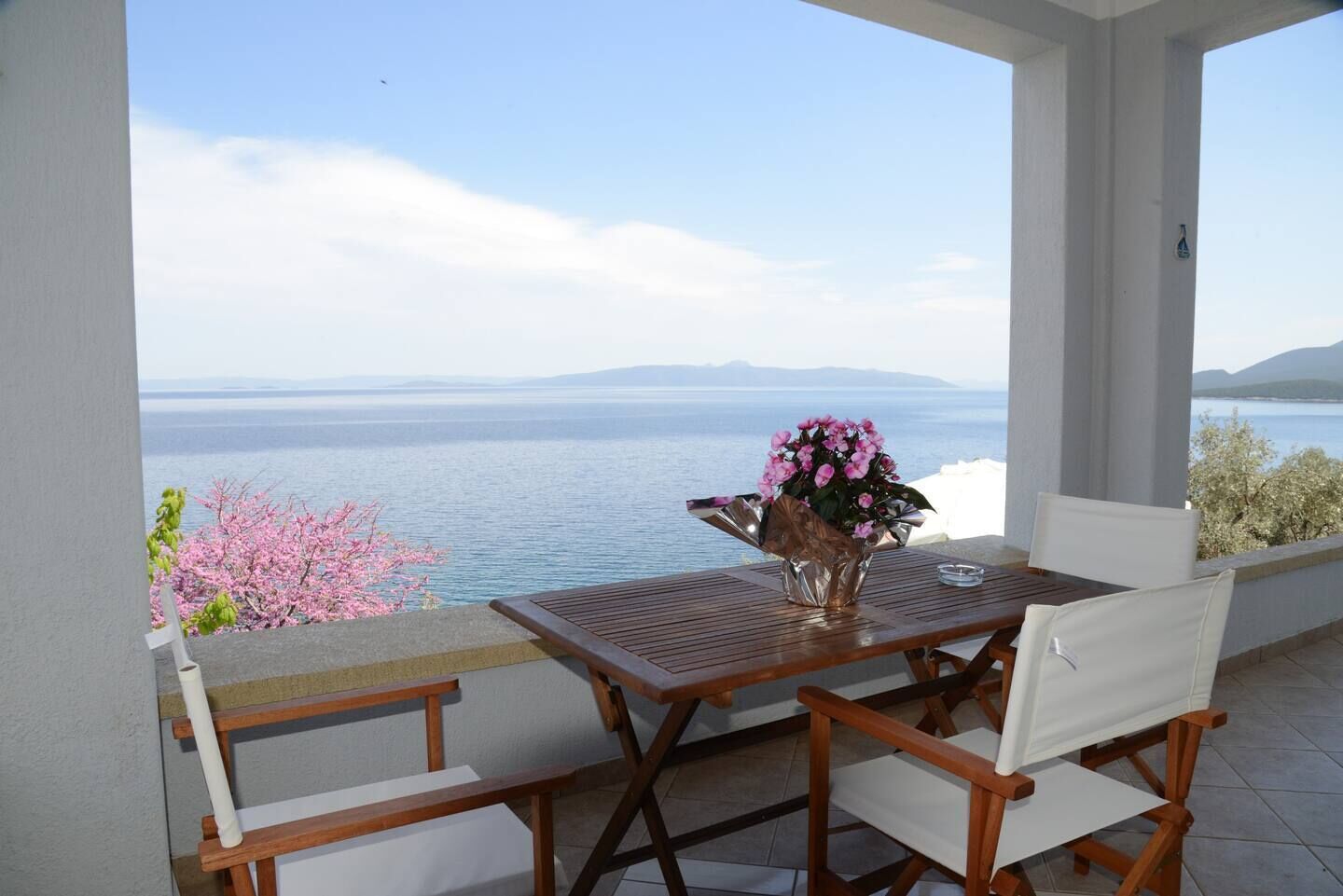 Ein Holztisch und -stühle auf einem Balkon mit Blick auf das Meer und die Berge.