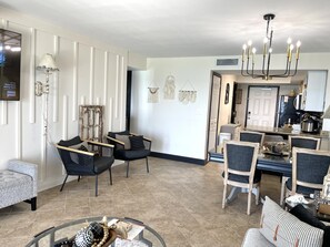 Un salon moderne avec un coin repas, agrémenté d’un lustre, d’une cheminée et d’une cuisine visible à travers une porte ouverte.